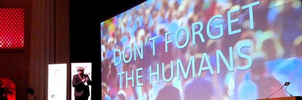 Gerard K Cohen, speaking at a conference, presenting in front of large screen that says 'Don't forget the humans!'